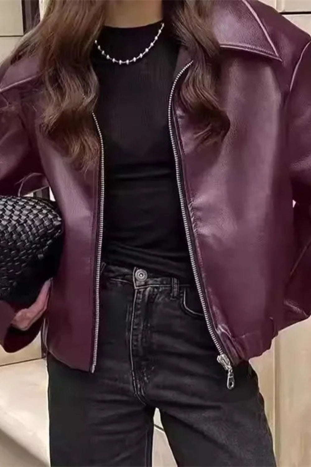 Person wearing a purple leather jacket and black pants, holding a black knitted bag.