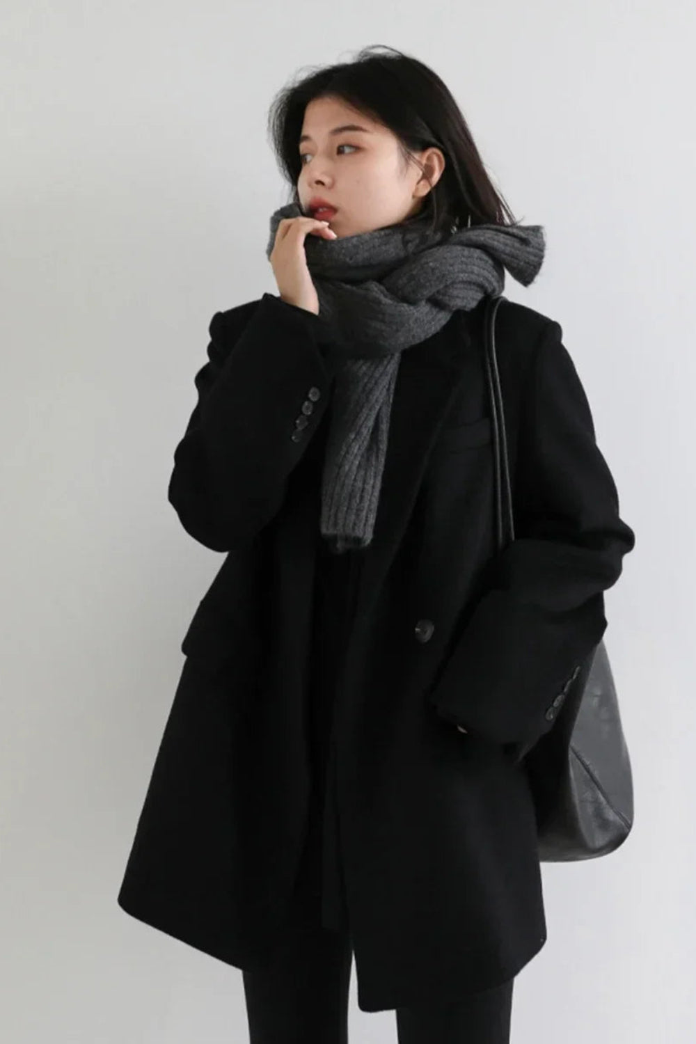 Person wearing a black coat and gray scarf against a white background