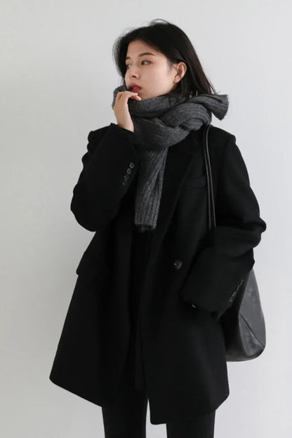 Person wearing a black coat and gray scarf against a white background