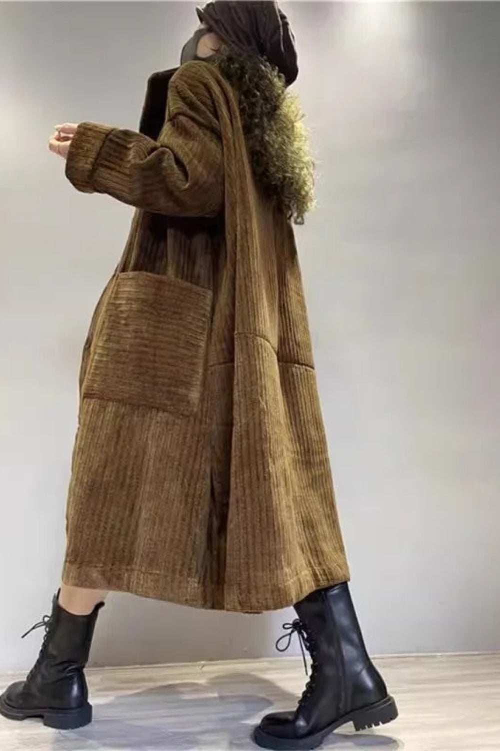 Person wearing a long brown coat and black boots against a plain background