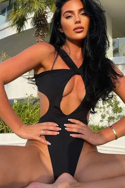 Woman in a black swimsuit posing outdoors with palm trees and buildings in the background