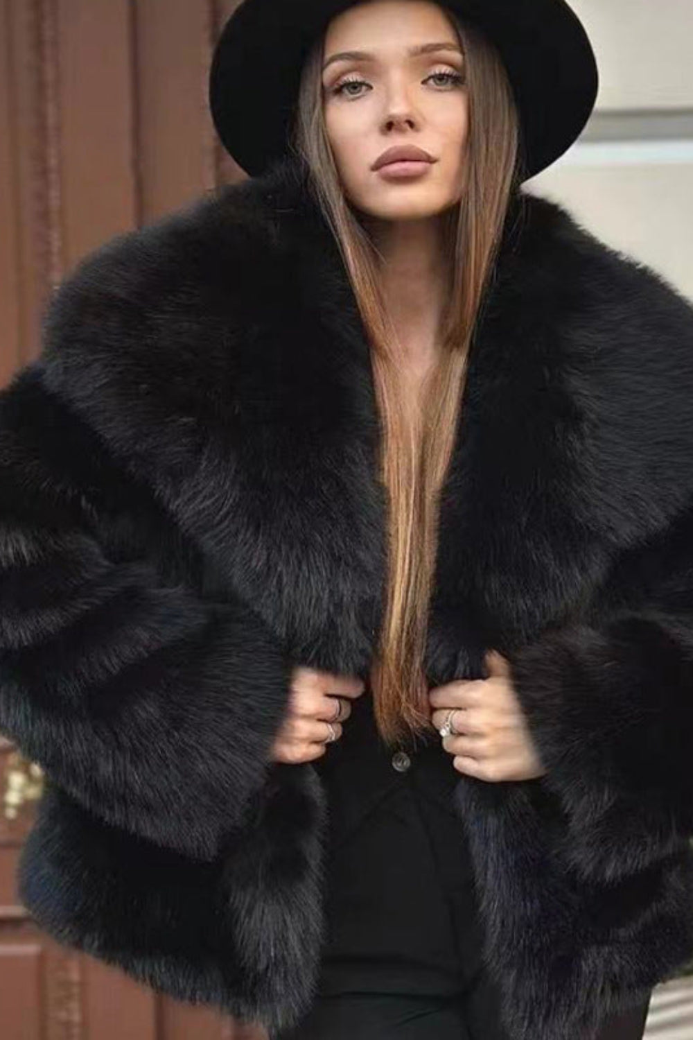 Woman wearing a black fur coat and hat in front of a building entrance.