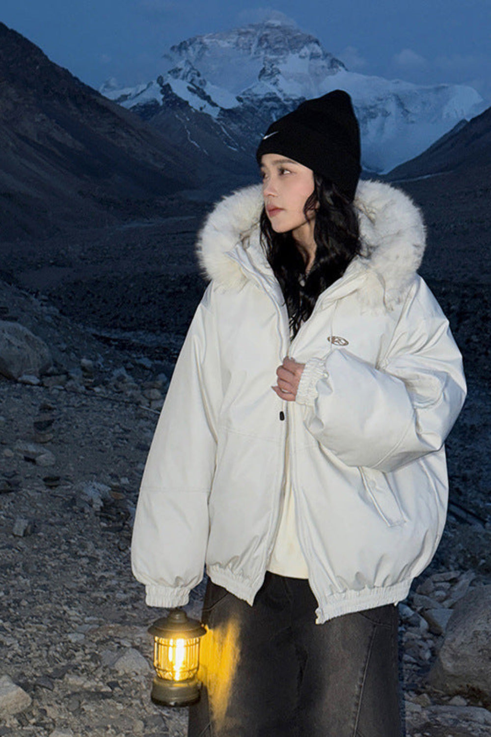 Person in a white parka with fur hood standing in a mountainous area at night.
