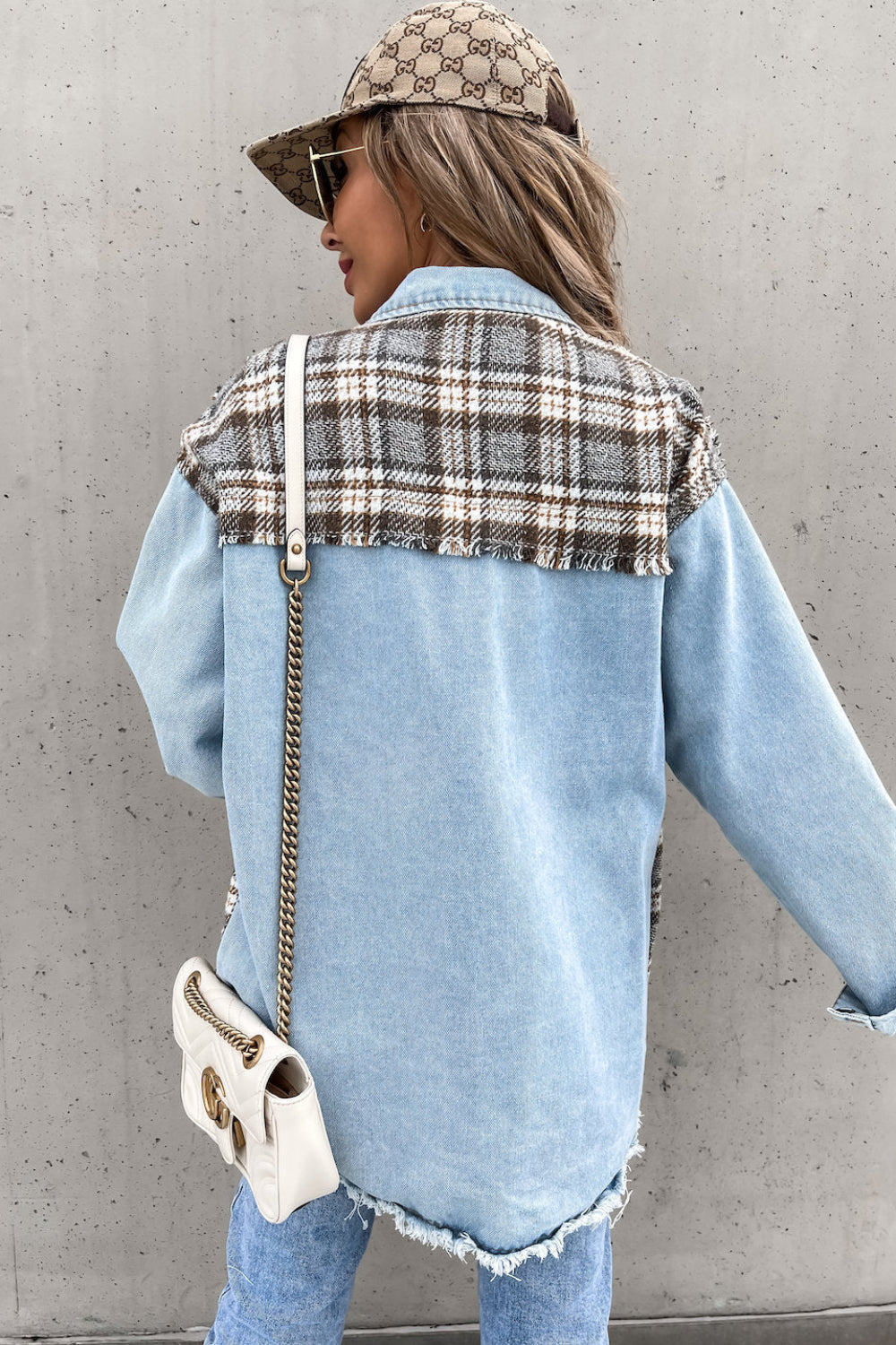 Person wearing a denim jacket with plaid pattern and Gucci cap against a gray wall.