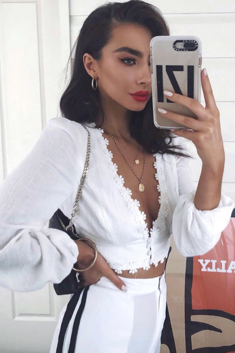 Woman taking a mirror selfie wearing a white outfit with a lace top.