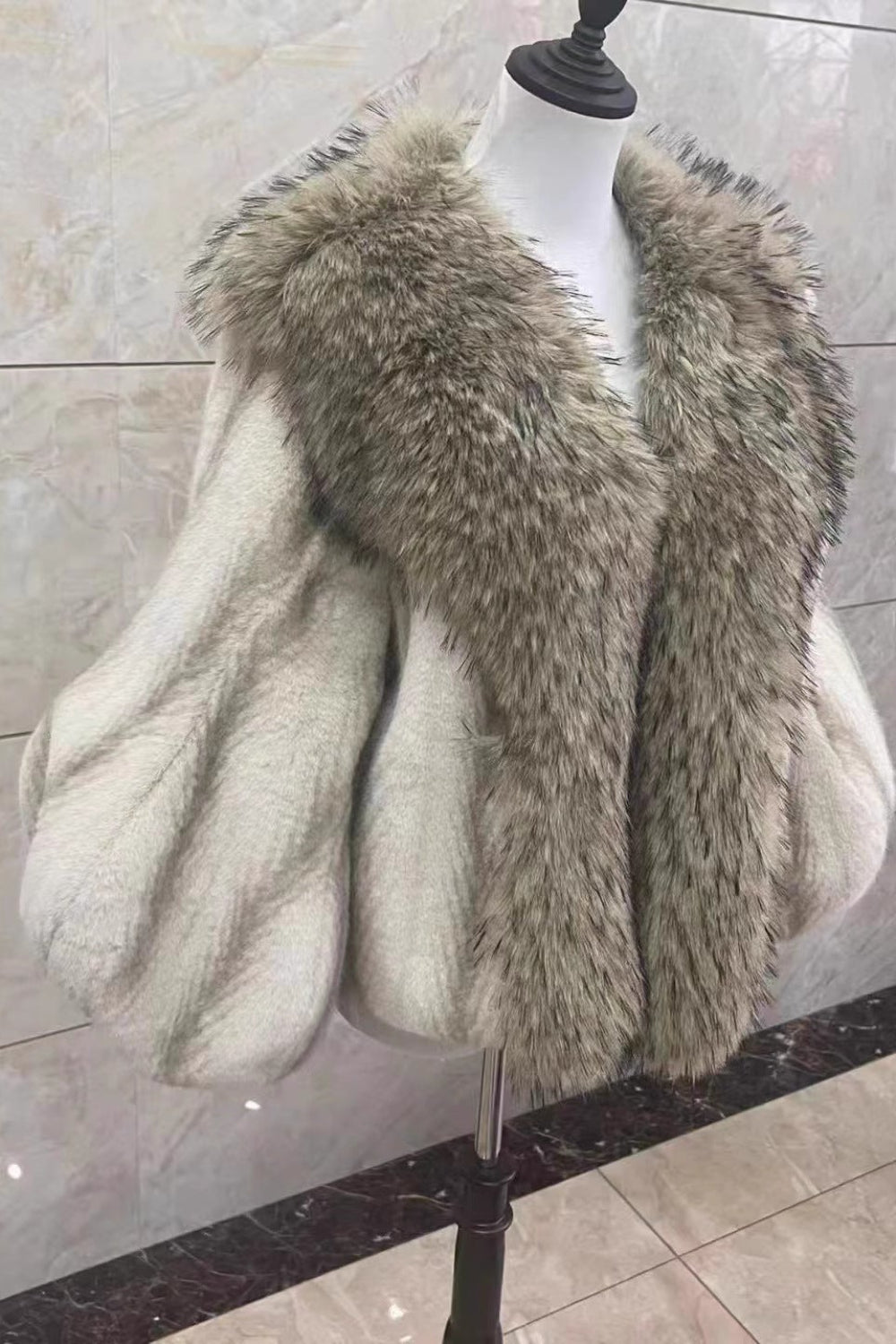Fur coat on a mannequin against a marble wall.