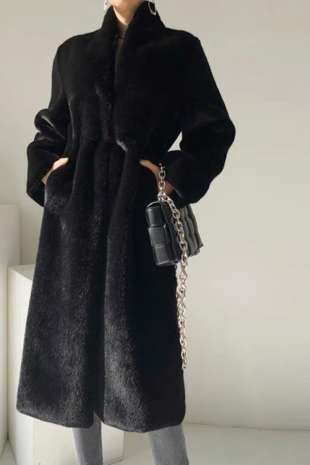 Person wearing a black coat holding a black handbag against a plain background