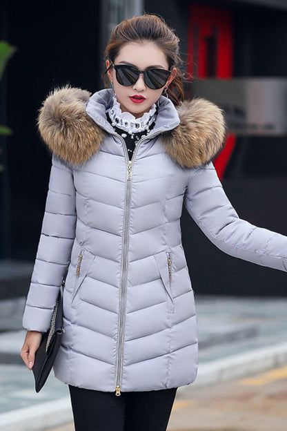 Woman wearing a light gray puffer jacket with a fur-lined hood outdoors.