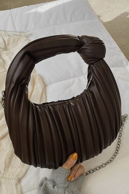 Brown pleated handbag with a chain detail held by a hand on a neutral background
