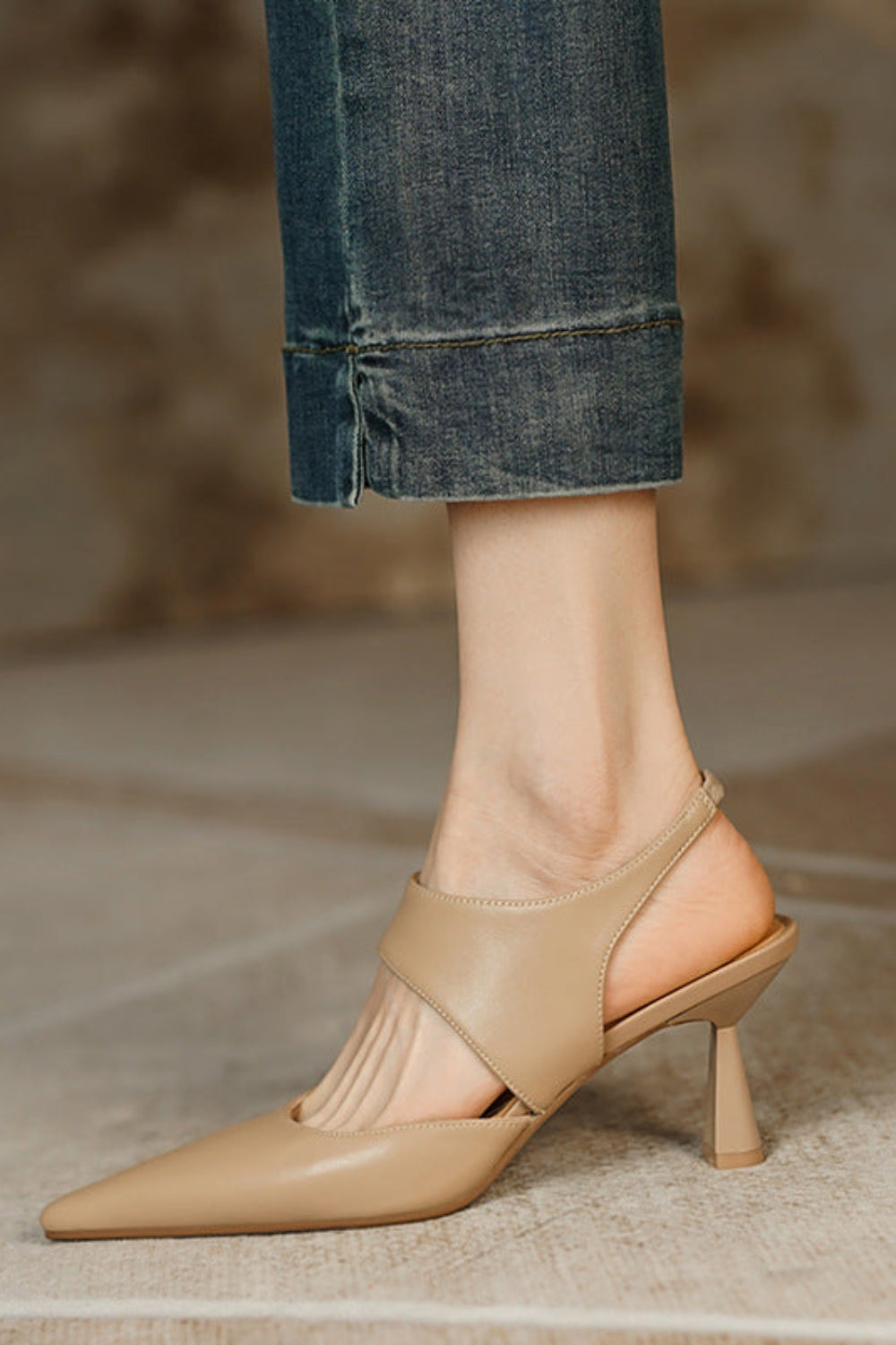 Beige high-heeled shoes worn with rolled-up jeans on a neutral background