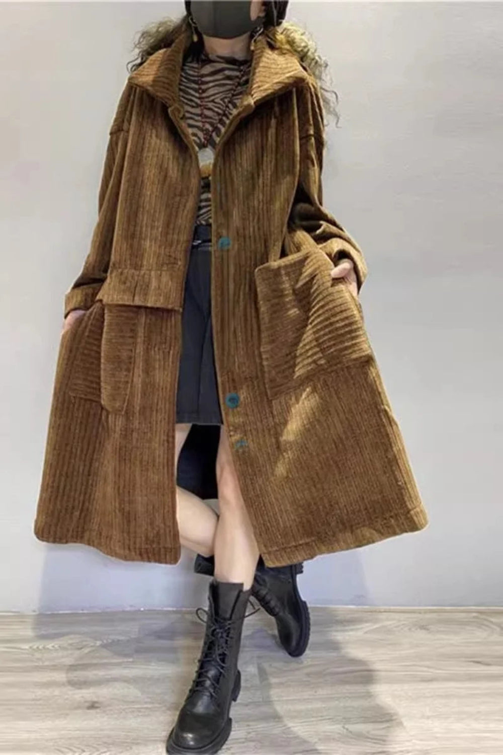 Person wearing a long brown corduroy coat with a plain background