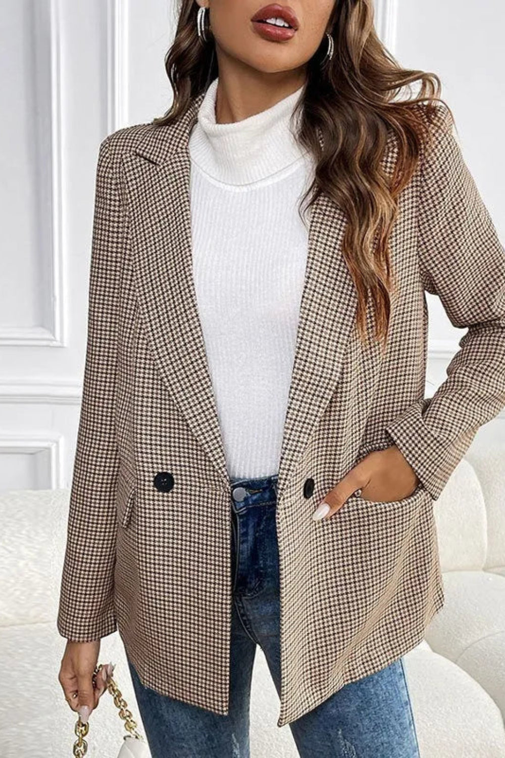 Woman wearing a plaid blazer over a white top and blue jeans in a minimalistic room.