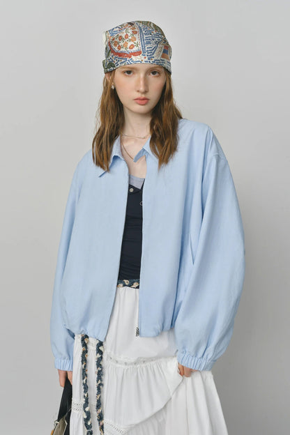 Person wearing a light blue shirt and patterned headscarf on a gray background