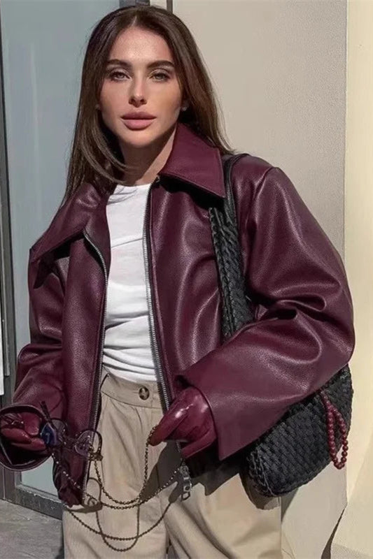 Woman wearing a purple leather jacket and gloves, standing against a neutral background.