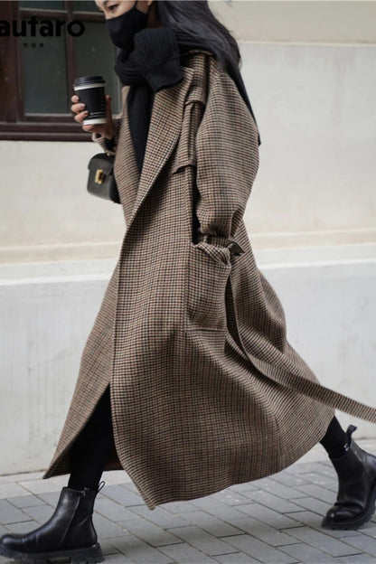 Person wearing a long plaid coat walking outdoors with a blurred background
