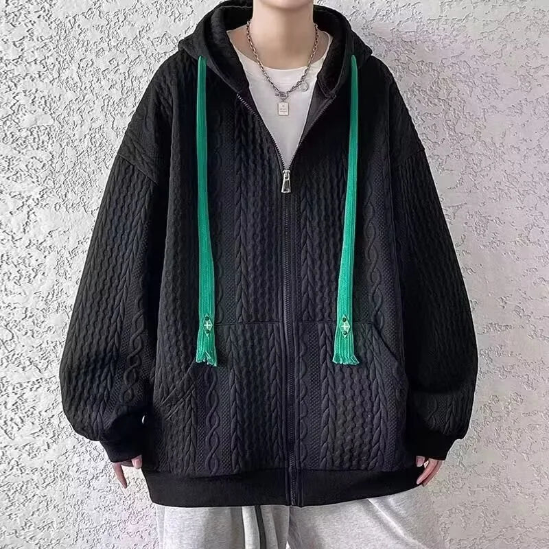 Person wearing a black textured hoodie with green drawstrings against a light gray background