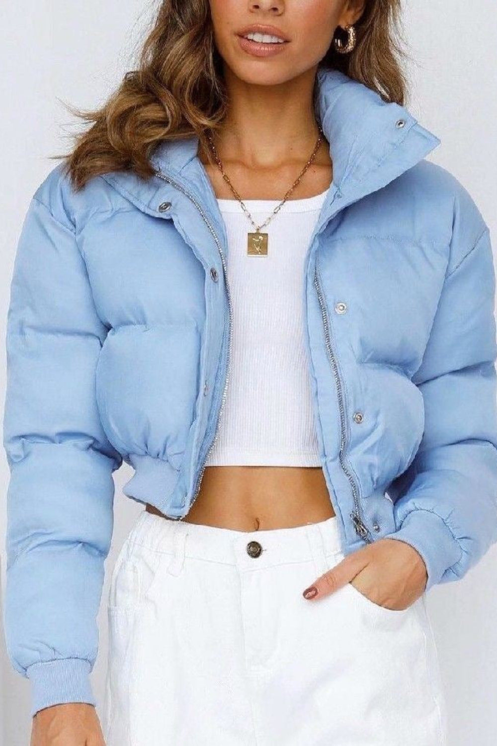 Woman wearing a light blue puffer jacket over a white top and pants on a white background