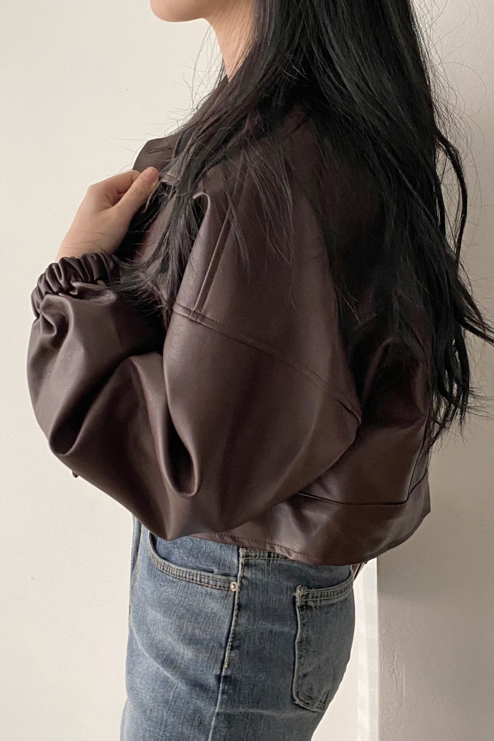 Person wearing a brown leather jacket and blue jeans against a plain background