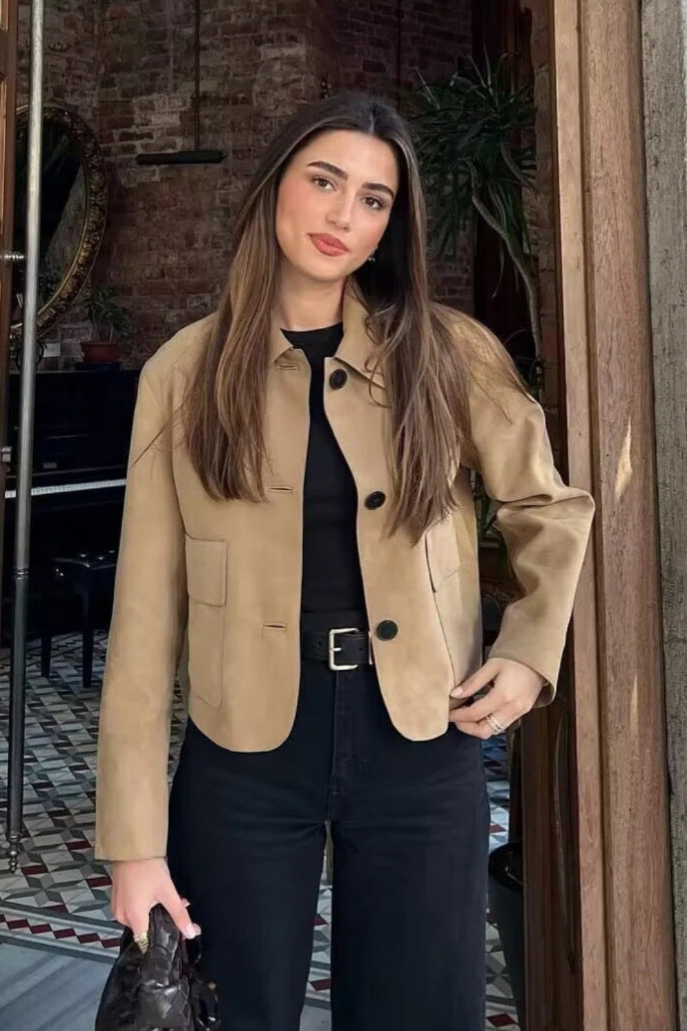 Woman in a beige jacket standing in a doorway with a brick wall background