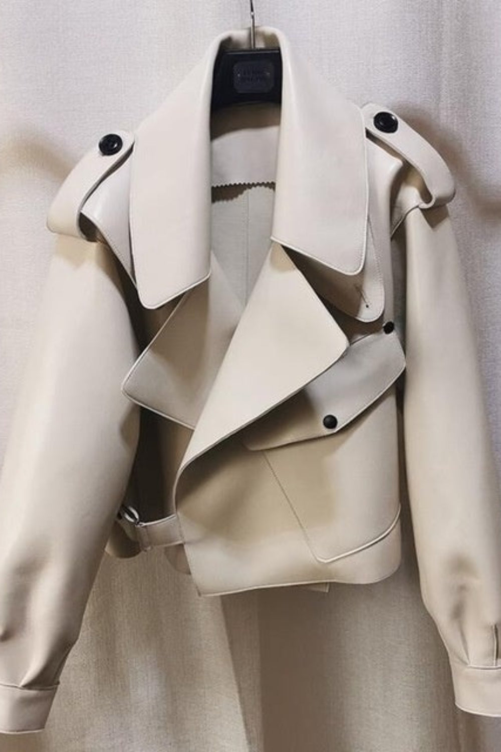 Beige leather jacket on a hanger against a neutral background
