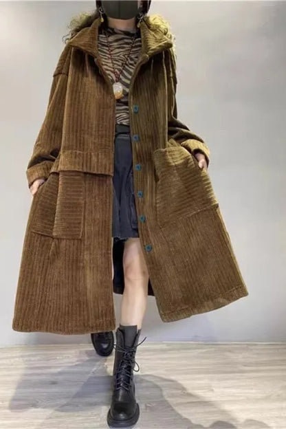 Person wearing a long brown corduroy coat with a hood on a plain background