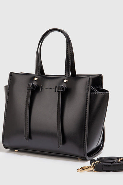 Black handbag with a detachable strap on a light gray background