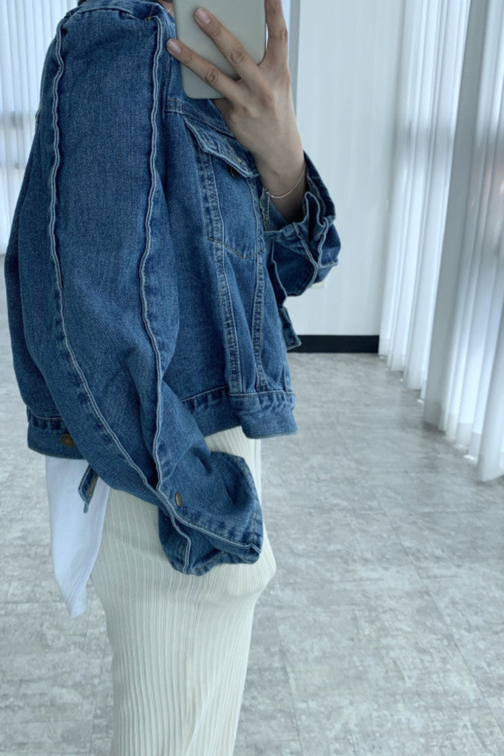 Person wearing an oversized denim jacket in a minimal indoor setting