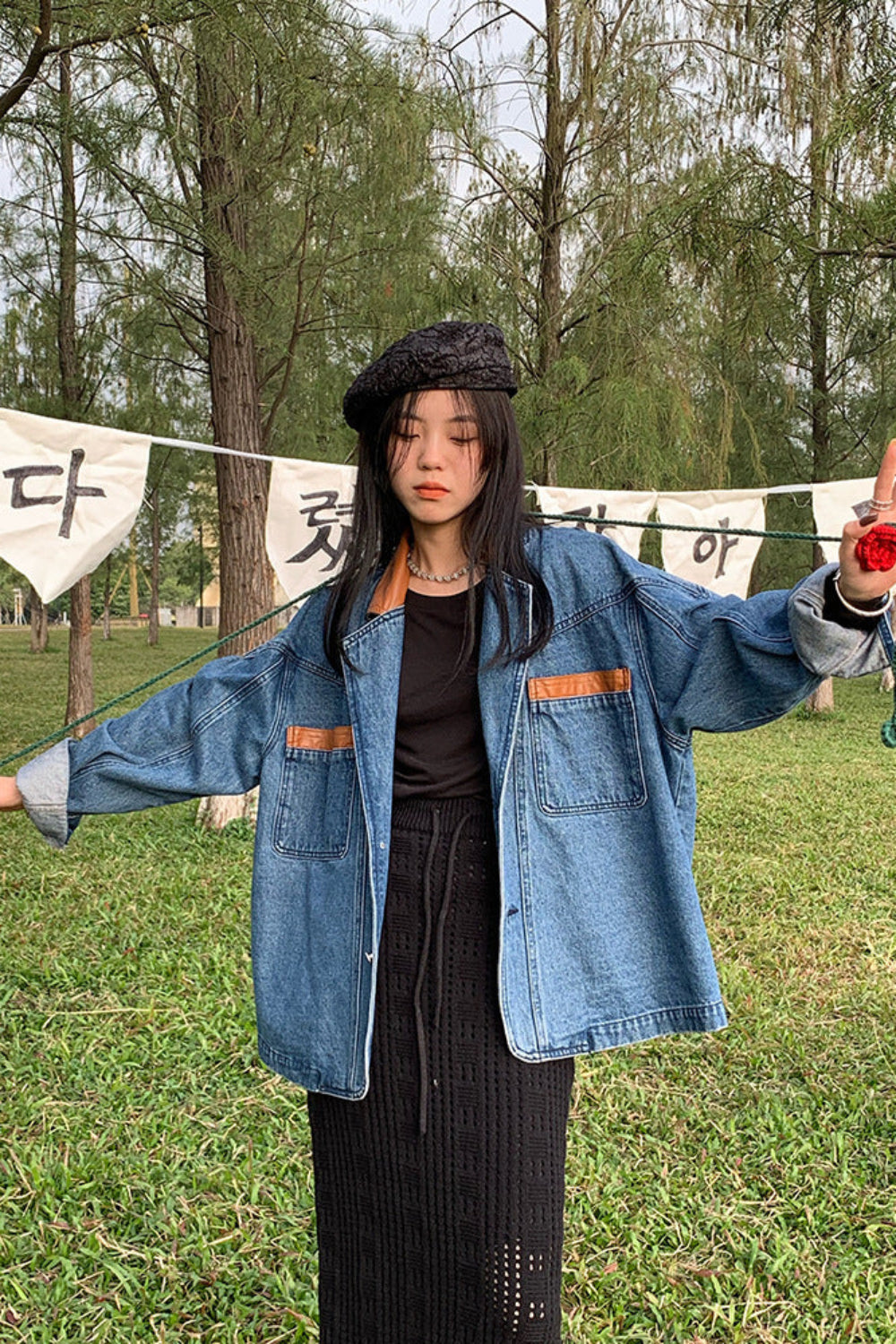 Person wearing a blue denim jacket in a park with trees and a banner in the background
