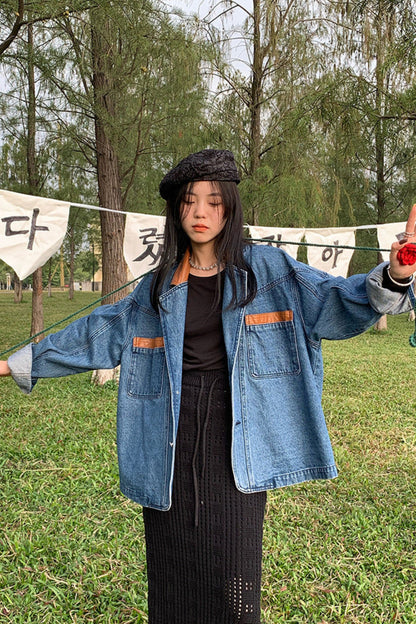 Person wearing a blue denim jacket in a park with trees and a banner in the background