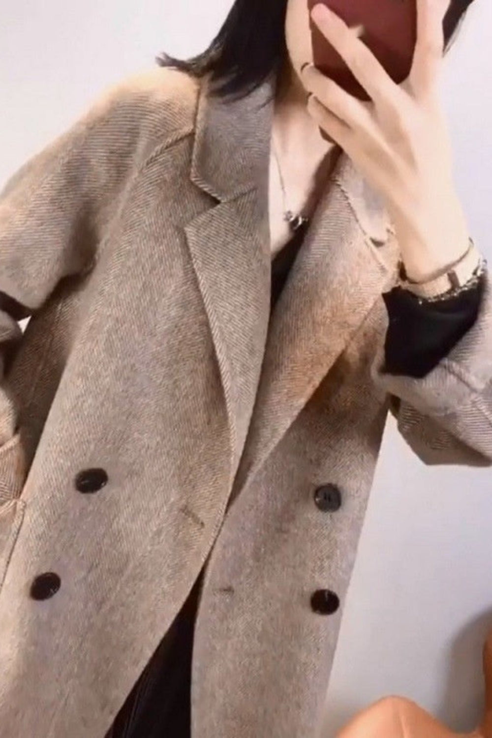 Person wearing a beige coat with black buttons against a plain background