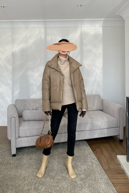 Person wearing a beige jacket, white turtleneck, black pants, and beige boots in a living room.