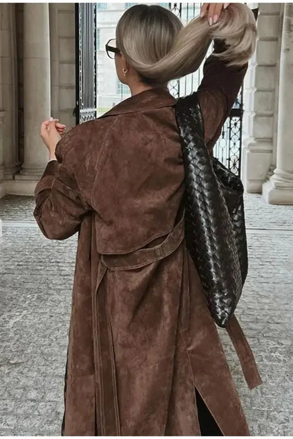 Person in a brown coat with a black backpack walking through an architectural setting.
