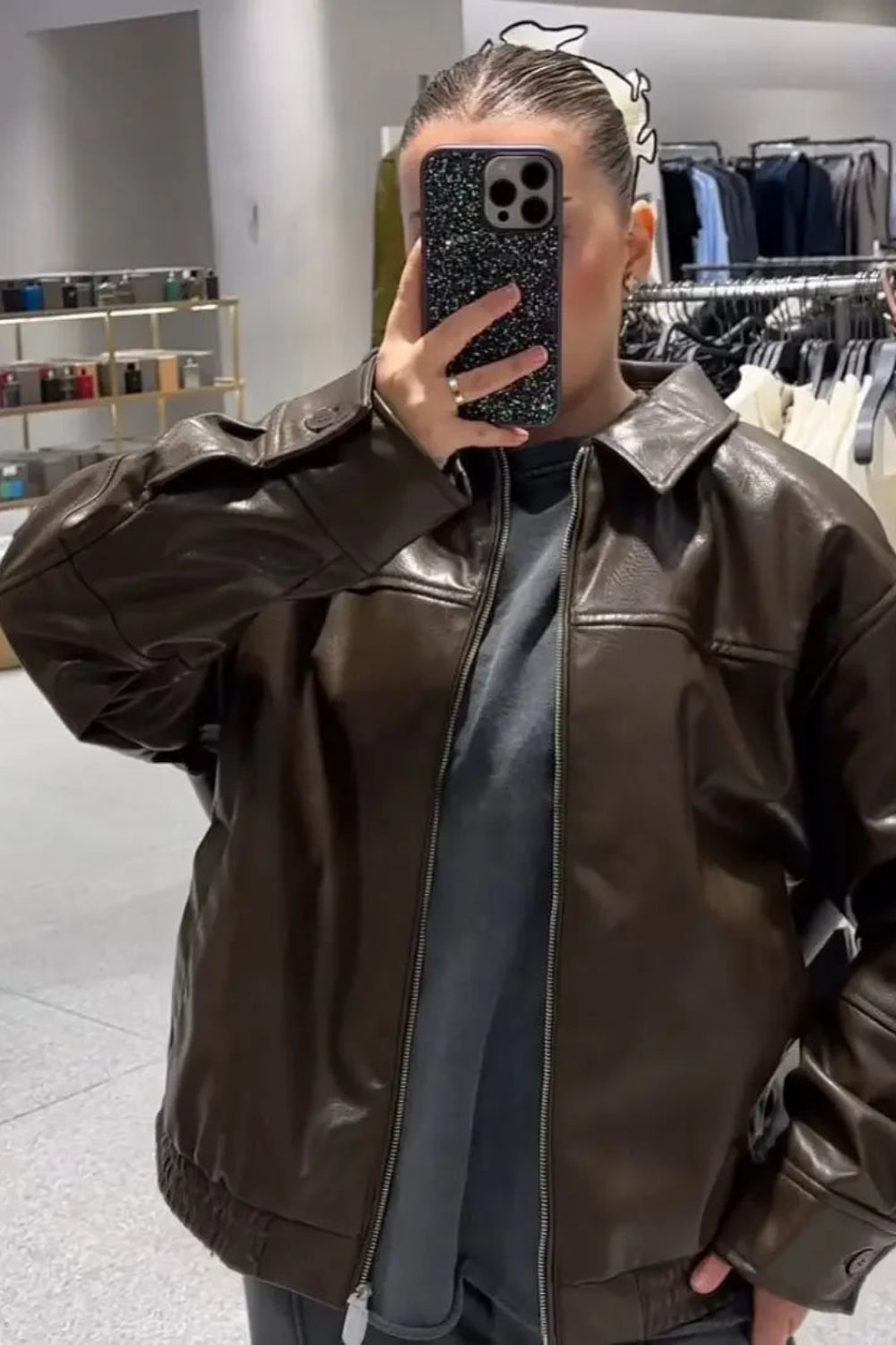 Person wearing a brown leather jacket in a clothing store.