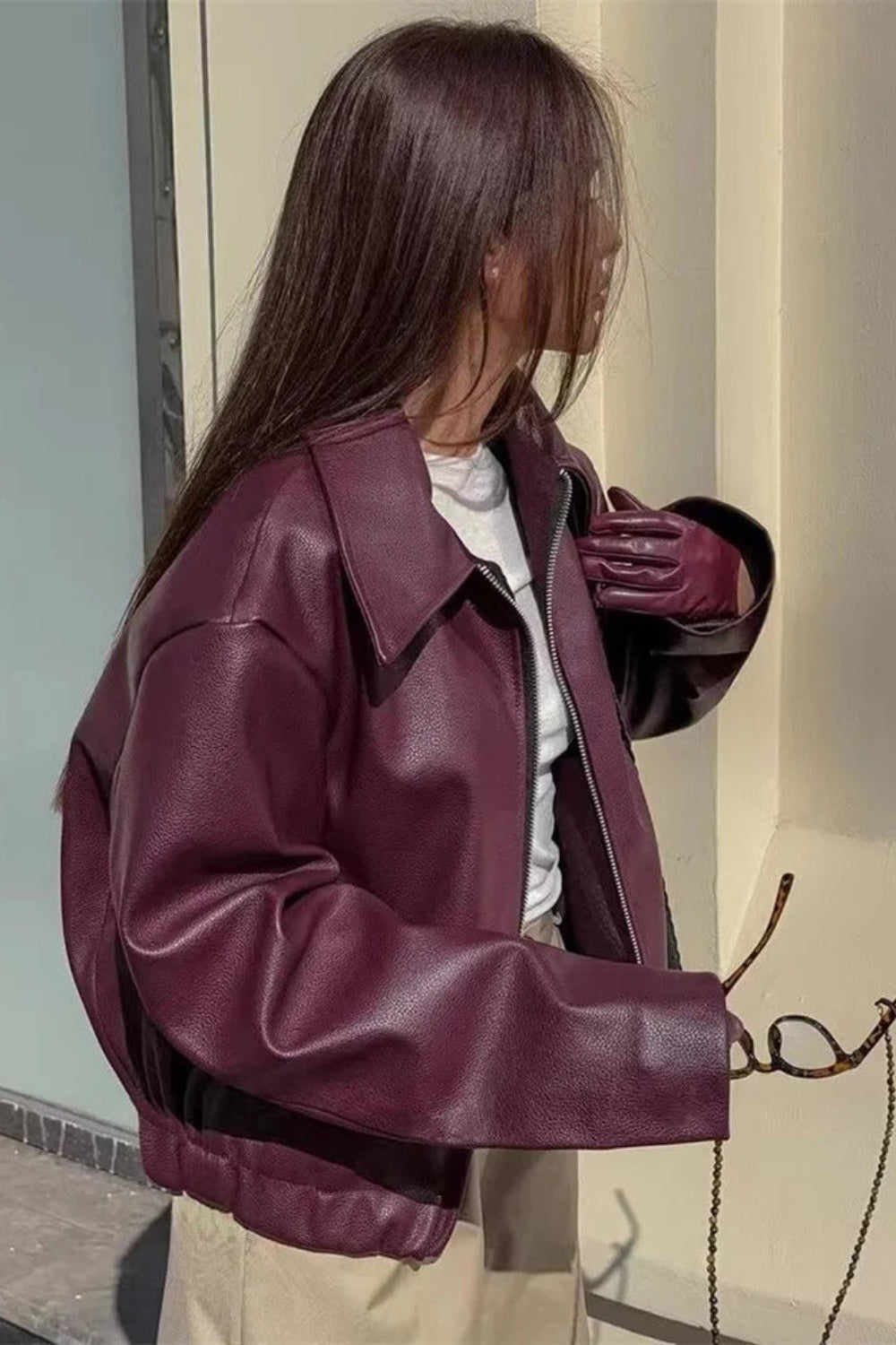 Person wearing a burgundy leather jacket standing against a neutral wall.