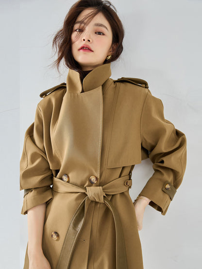 Woman wearing a beige trench coat against a plain background