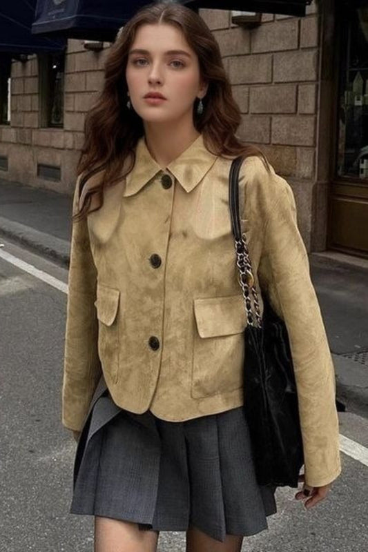 Woman in a beige jacket and gray skirt standing on a city street.