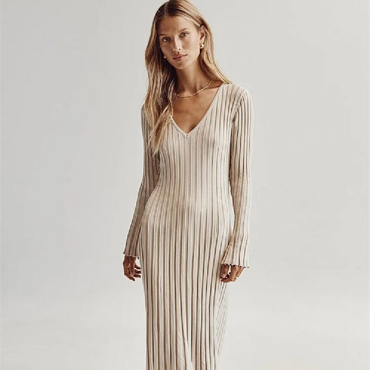 Woman wearing a long, light-colored dress with thin stripes against a plain background