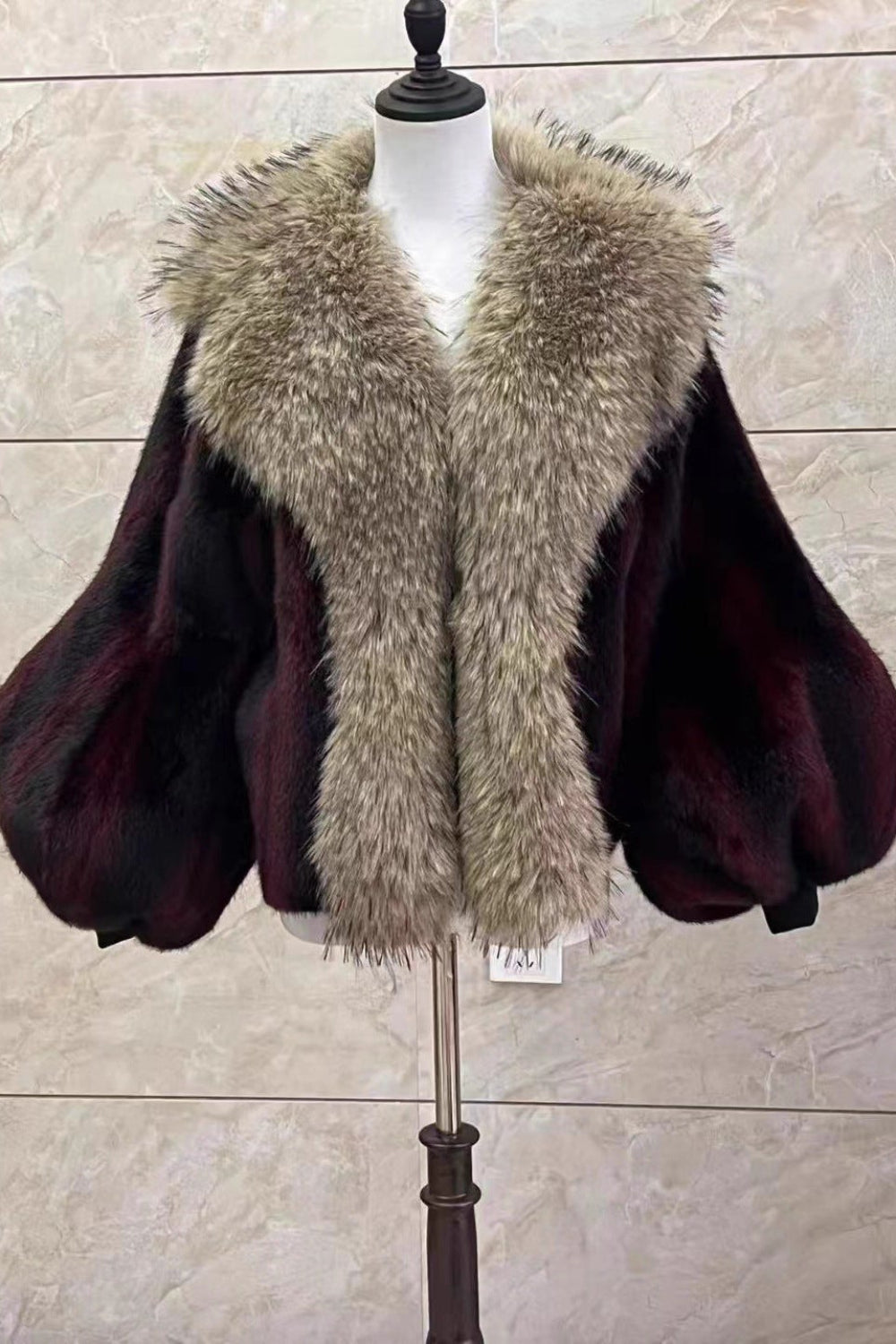 Mannequin wearing a dark purple cape with a fur collar against a beige wall.