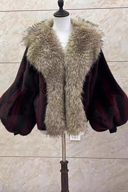 Mannequin wearing a dark purple cape with a fur collar against a beige wall.