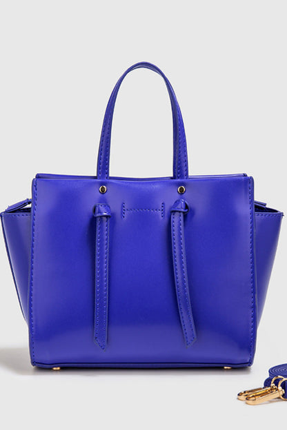 Blue handbag with matching strap on a light gray background