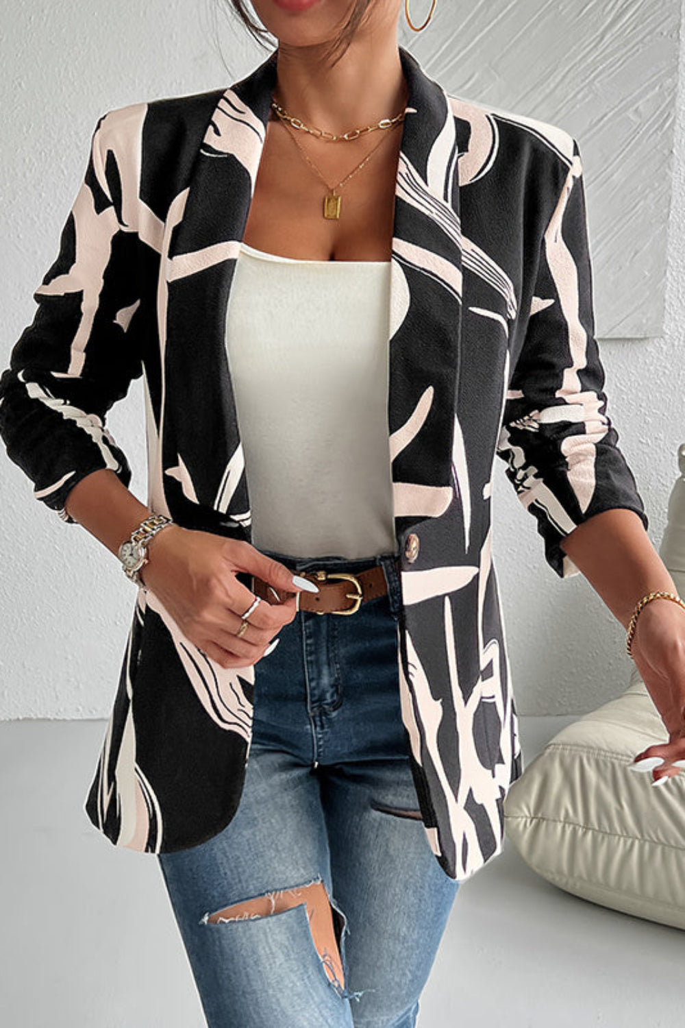 Woman wearing a patterned blazer over a white top and jeans in a minimalistic room.