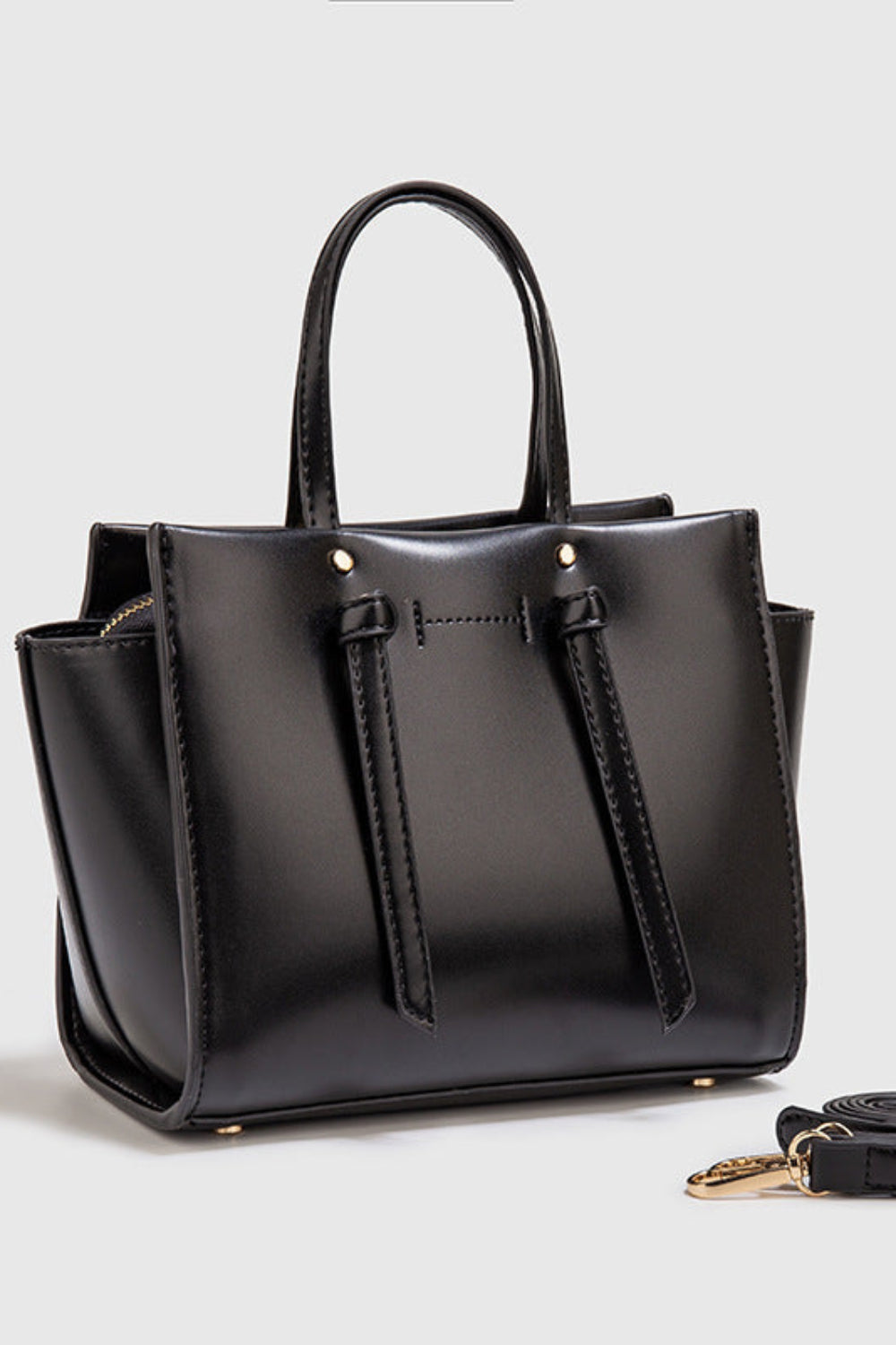 Black handbag with a matching strap on a light gray background