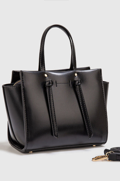 Black handbag with a matching strap on a light gray background