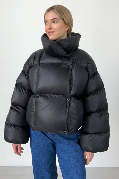 Person wearing a black puffer jacket and blue jeans on a white background