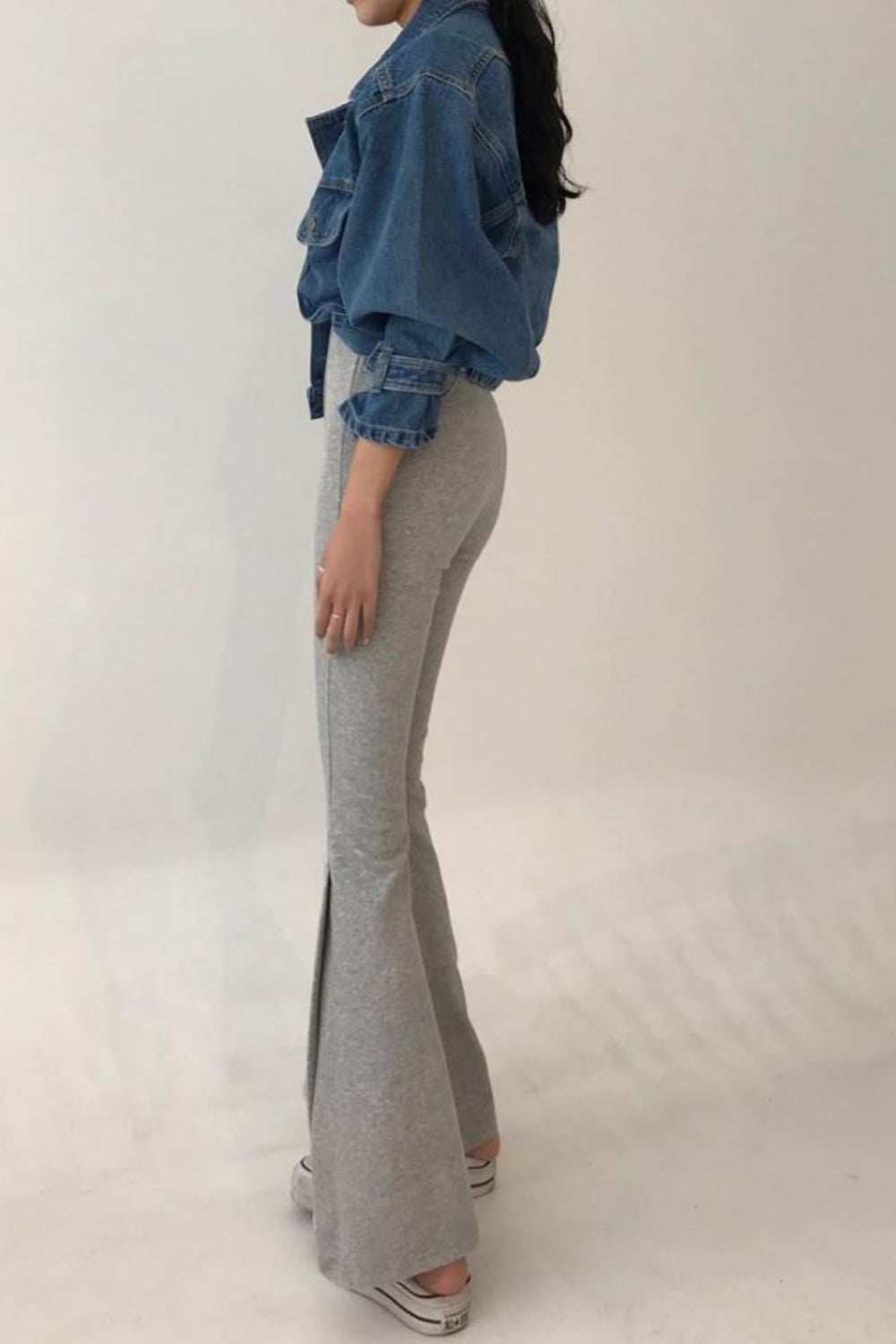 Person wearing a blue denim jacket and gray flared pants on a white background