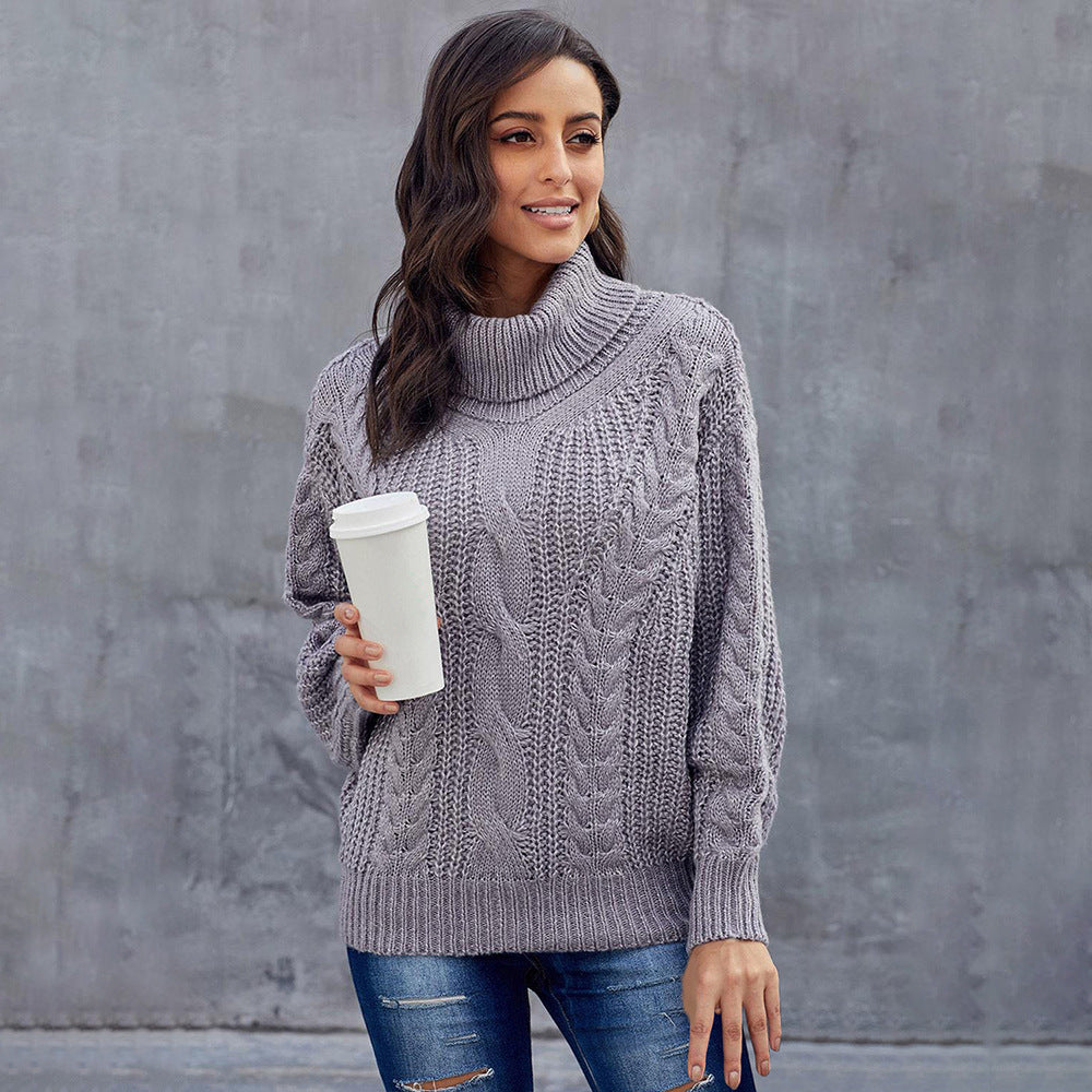 Woman wearing a gray cable knit sweater holding a white cup against a gray wall.