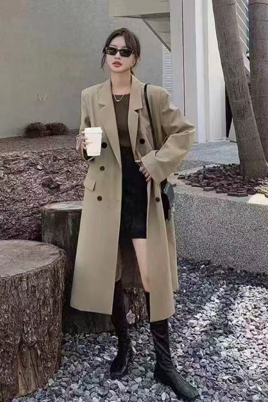 Woman in a beige trench coat holding a coffee cup outdoors.