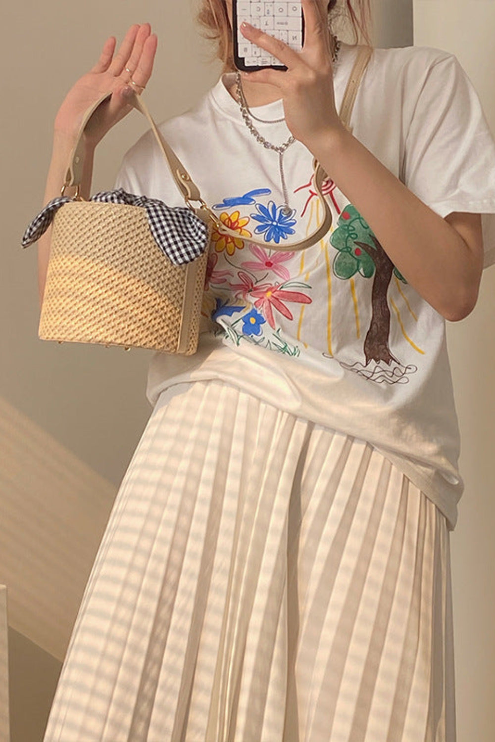 Person holding a woven handbag, wearing a colorful graphic t-shirt and light-colored skirt.