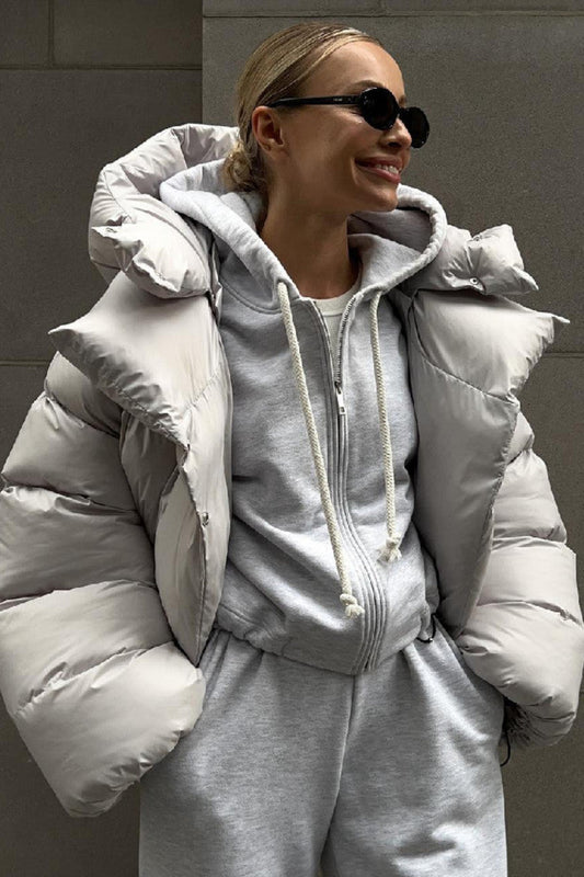 Person wearing a gray puffer jacket and matching outfit against a gray wall.