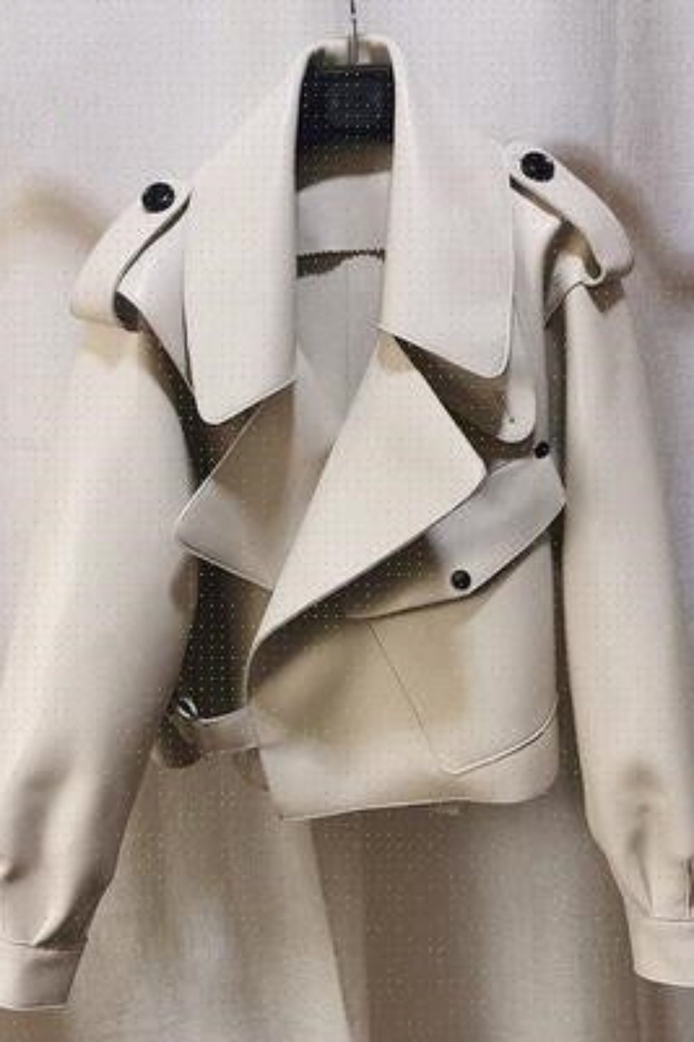 Beige leather jacket on a hanger against a neutral background